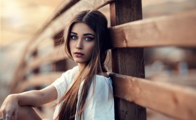 Beautiful girl sitting, leaning to wooden fence